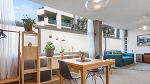 Un salon moderne avec une table à manger en bois, des chaises, un canapé et un balcon agrémenté de plantes.