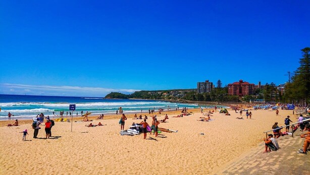 A crowded beach with people sunbathing and swimming, a lifeguard tower, and buildings in the background. - Art Deco Apartment Meters Away From The Beach (Sydney)
