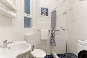 A bathroom with a white sink, toilet, and glass shower enclosure. - Art Deco Apartment Meters Away From The Beach (Sydney)