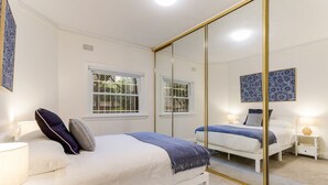 A bedroom with a large mirror, a bed with pillows, a nightstand, and a window. - Art Deco Apartment Meters Away From The Beach (Sydney)