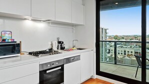 A modern kitchen with white cabinets, a gas stove, a microwave, and a dishwasher. - Bright Apartment With City Views in Trendy Locale (Melbourne)