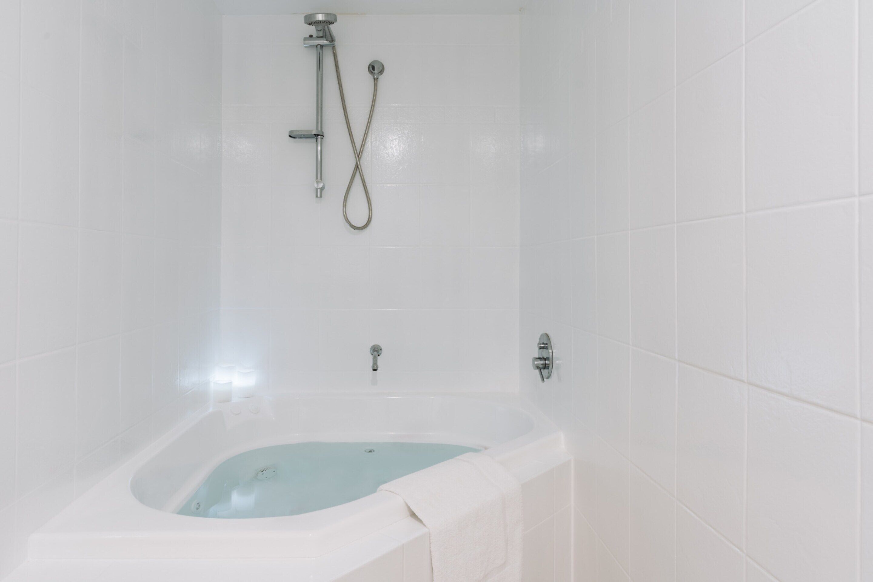 A white-tiled bathroom with a bathtub, shower, and two faucets.