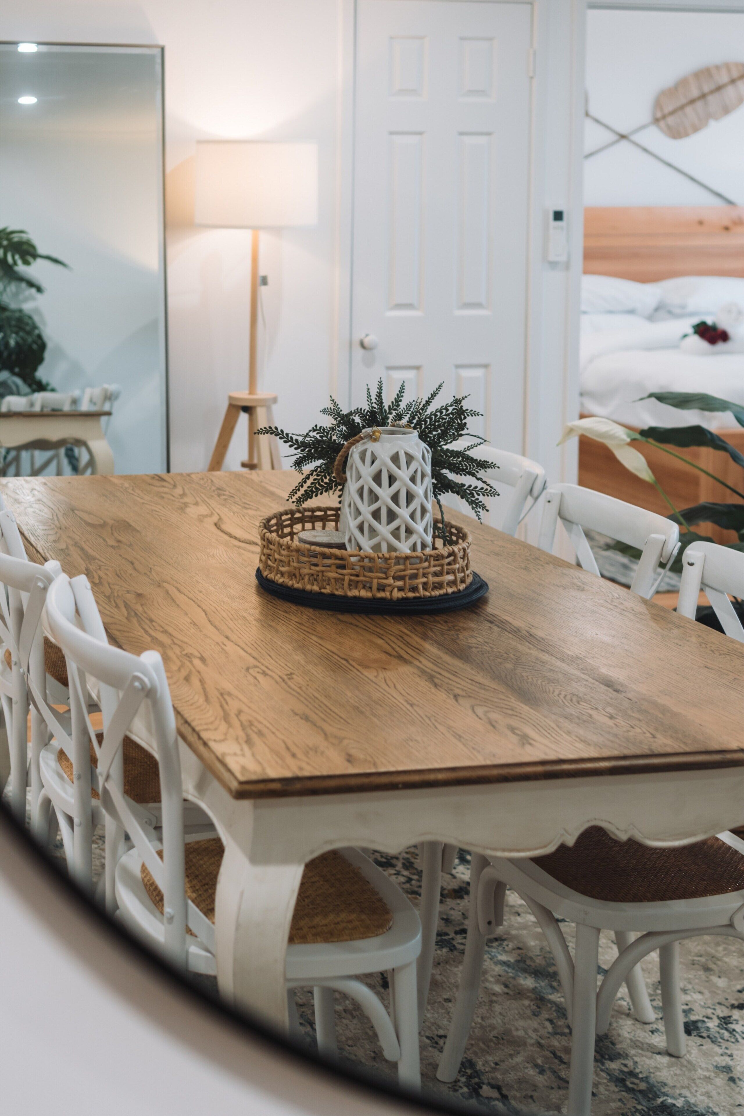 A dining area with a wooden table, white chairs, a woven centerpiece, and a lamp.