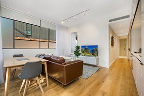 Uma sala de estar moderna com uma mesa de jantar de madeira, um sofá de couro marrom e uma TV fixada na parede.