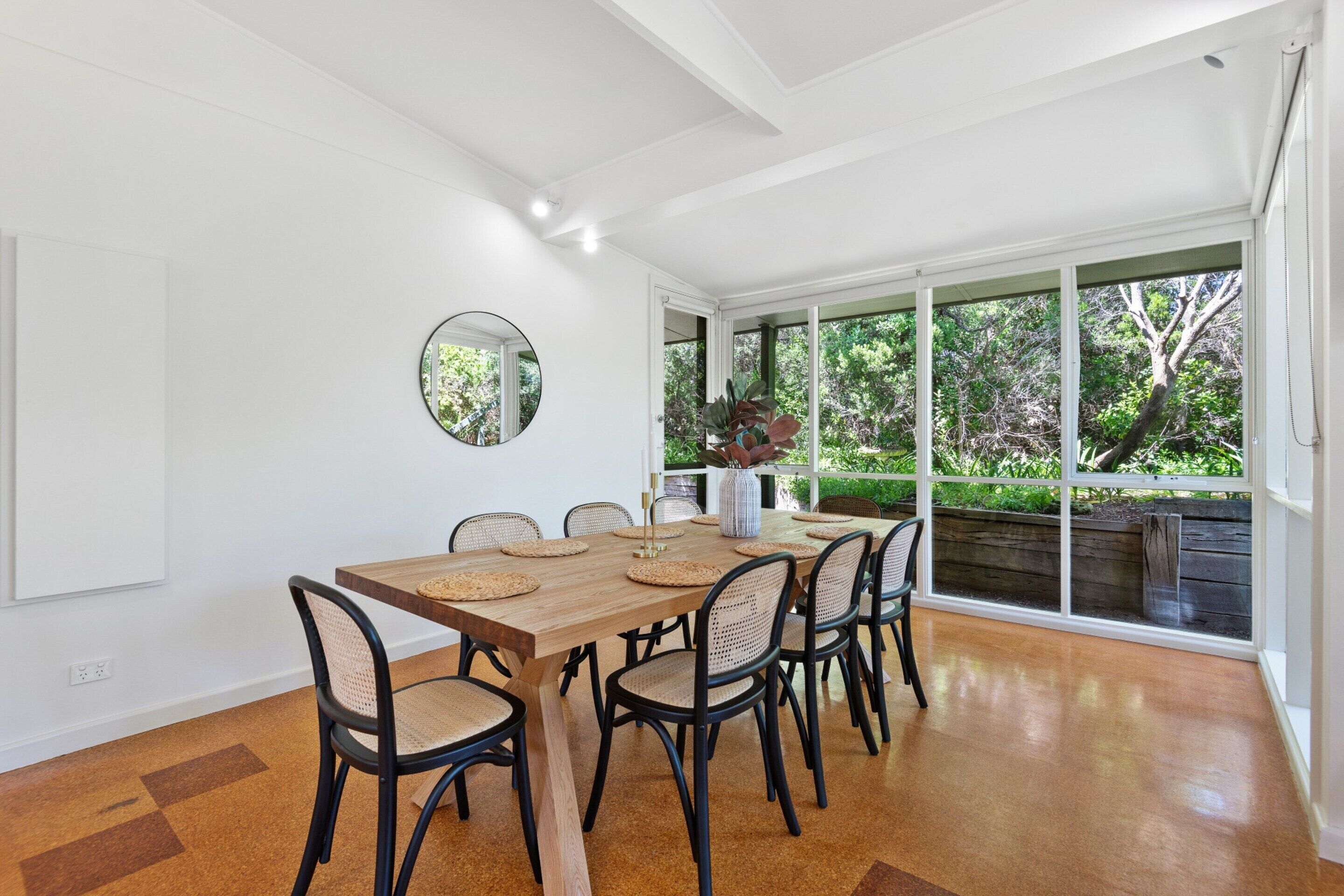 A dining area with a wooden table, black chairs, and a large window with a view of greenery.