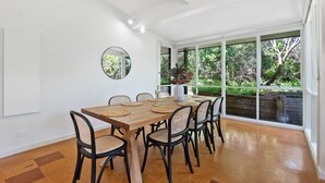 A dining area with a wooden table, black chairs, and a large window with a view of greenery. - Spacious Coastal 4-bed Steps From the Sand (Melbourne)