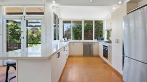 A modern kitchen with white cabinetry, a stainless steel refrigerator, and a dishwasher. - Spacious Coastal 4-bed Steps From the Sand (Melbourne)