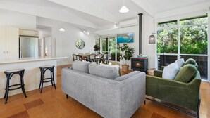 A modern living room with a grey sofa, a green armchair, and a dining area with a table and chairs. - Spacious Coastal 4-bed Steps From the Sand (Melbourne)