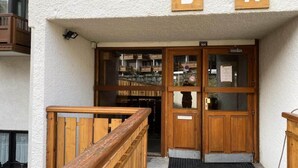 A wooden entrance with a glass door, a wooden railing, and a balcony with a view of a building in the background. - VAL Thorens Rental: Studio for 4 on the Edge of the Slopes (Les Belleville)