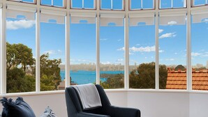A room with a large bay window offering a view of a coastal cityscape. - Huge Harbour View Apartment In Historic Home (Sydney)