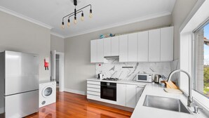 A modern kitchen with white cabinets, a stainless steel refrigerator, a built-in oven, and a large window providing a view. - Huge Harbour View Apartment In Historic Home (Sydney)