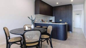 Una cocina moderna con armarios oscuros, una isla central y un comedor con sillas de mimbre.