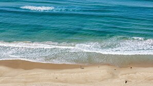 A beach with clear turquoise water, a sandy shore, and a few people walking. - Wonderful 2-bed With Pool, Gym & Scenic Views (Gold Coast)