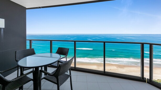 A balcony with a glass table and chairs, overlooking a beach and ocean. - Wonderful 2-bed With Pool, Gym & Scenic Views (Gold Coast)