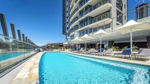 A swimming pool with lounge chairs and umbrellas, surrounded by a modern building with balconies. - Wonderful 2-bed With Pool, Gym & Scenic Views (Gold Coast)