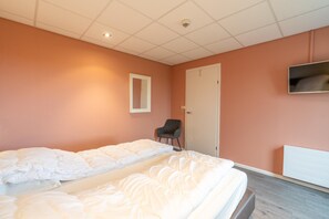 A hotel room with a bed, a chair, a television, and a door.