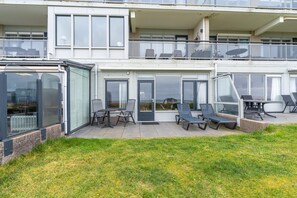 A modern two-story residential building with a covered patio area featuring outdoor furniture. - Sea View Apartment (De Koog)