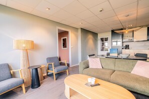 A modern living room with a sofa, chairs, a coffee table, and a dining area with a kitchen in the background.