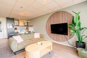 A modern living room with a sofa, coffee table, and a TV mounted on a wooden panel wall. - Sea View Apartment (De Koog)