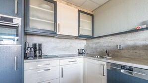 A modern kitchen with white cabinets, a built-in oven, a coffee maker, and a dishwasher. - Sea View Apartment (De Koog)