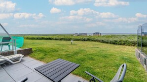 A patio area with a view of the sea, a swimming pool, and a grassy lawn. - Sea View Apartment (De Koog)