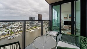 A balcony with a view of a river and buildings, a table with chairs, and a room with a TV and furniture. - 2-bed With Harbour Views & Outstanding Amenities (Melbourne)