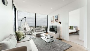 A modern living room with a sofa, coffee table, and a view of the city through large windows. - 2-bed With Harbour Views & Outstanding Amenities (Melbourne)