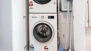 A compact laundry room with two stacked washing machines, a mop, and a laundry basket. - 2-bed With Harbour Views & Outstanding Amenities (Melbourne)