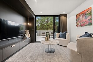 A modern living room with a flat-screen TV, a round coffee table, and a sofa. - Braddon Studio With Parking & BBQ (Canberra)