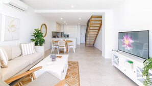 A modern living room with a sofa, coffee table, TV, and a staircase leading to a kitchen. - Lavish Coastal 2-bed With Stunning Ocean Views (Batemans Bay)