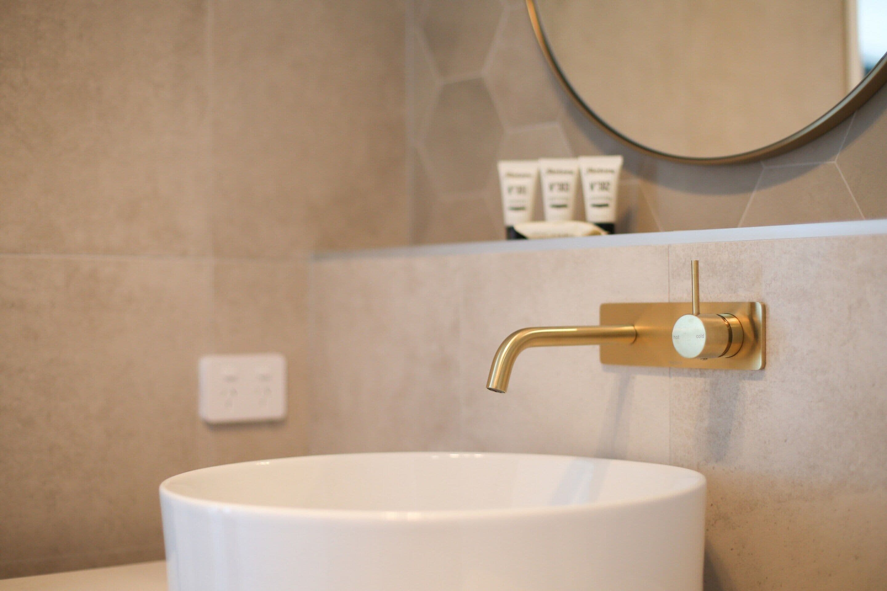 Ein Badezimmer mit einem weißen Waschbecken, einem goldenen Wasserhahn und einem Spiegel darüber.