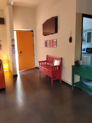 A hallway with a red bench, a green table, and a door leading to a room.