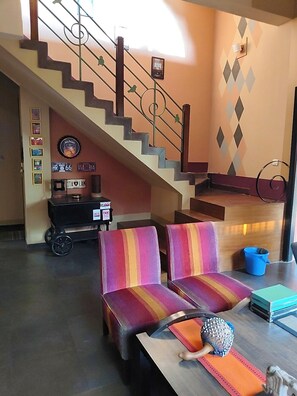 A living room with a staircase, striped sofas, a coffee table, and a small cart with a sign.