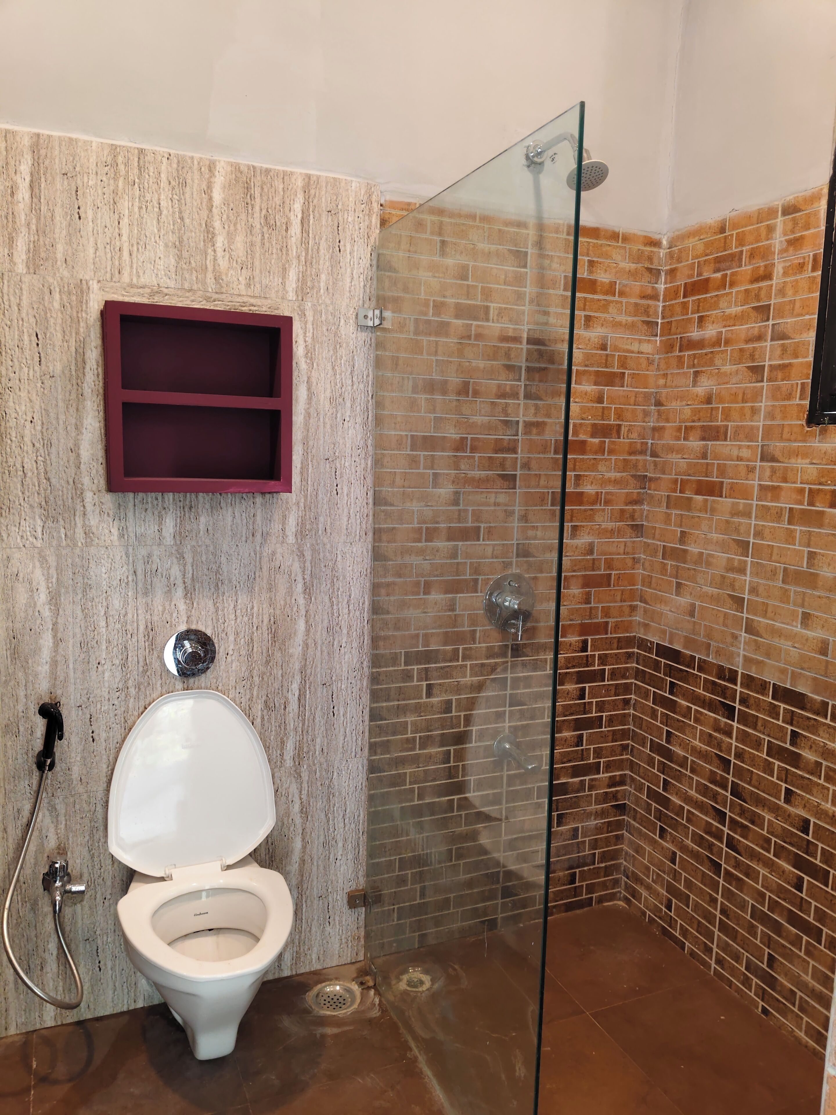 Une salle de bain avec une douche à parois de verre, un mur en marbre, des toilettes blanches et un meuble à pharmacie rouge.