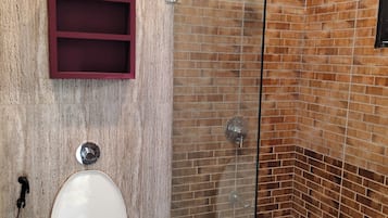 Une salle de bain avec une douche à parois de verre, un mur en marbre, des toilettes blanches et un meuble à pharmacie rouge.