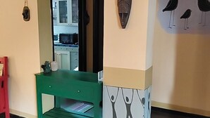 Un pasillo con un banco verde, un espejo y detalles decorativos en la pared, incluyendo un mural de un pájaro y una máscara.