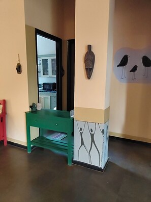A hallway with a green bench, a mirror, and wall art including a bird mural and a mask.