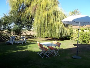 Une terrasse avec une table et des chaises, un parasol blanc et un saule pleureur.