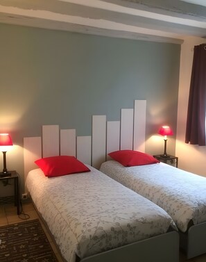 Une chambre avec deux lits, chacun agrémenté d’un oreiller rouge, une table de chevet avec une lampe et un radiateur fixé au mur.