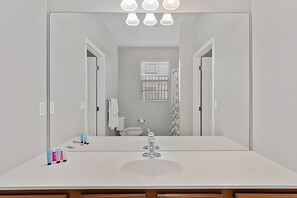 Casa de banho com um espelho grande, lavatório branco e janela com persianas.