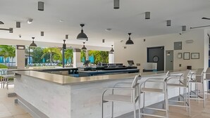 Uma área de bar moderna com ilha central, banquetas, iluminação pendente e vista para o exterior.