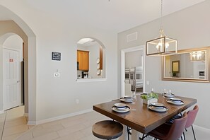 Uma sala de jantar moderna com uma mesa de madeira posta para quatro pessoas, um lustre pendurado e um espelho grande na parede.