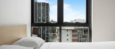 A hotel room with a large window, a bed, and a view of buildings and a river.