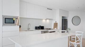 A modern kitchen with white cabinetry, a built-in microwave, a stove, and a dining area with white chairs.