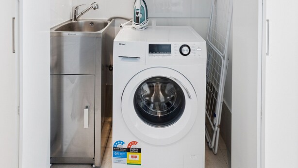 A compact laundry room with a washing machine, a small sink, and a wall-mounted dryer. - 52nd Floor With Panoramic Views of Brisbane City (Brisbane)