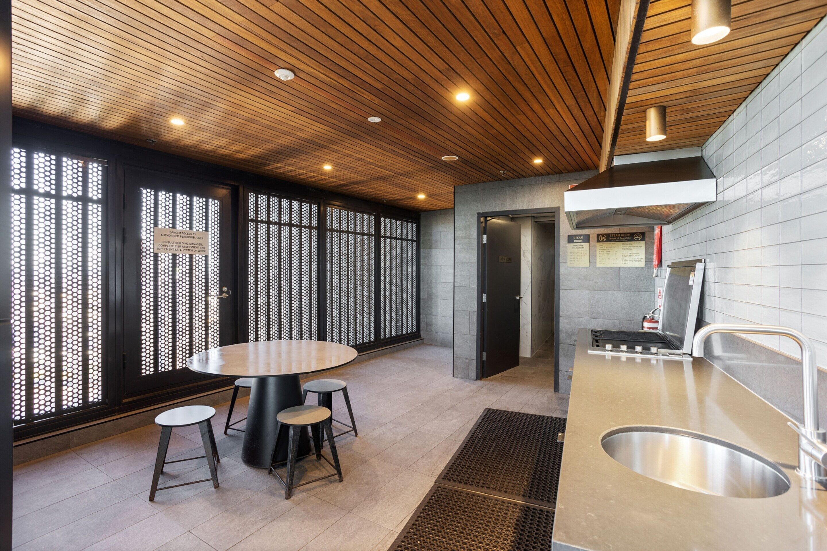 A modern kitchen with a round table and stools, a sink, and a wooden ceiling.