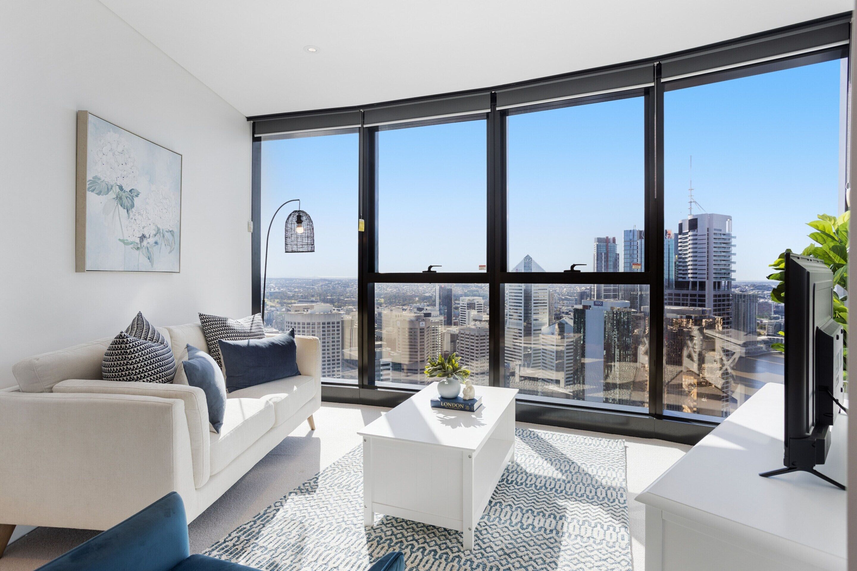 A modern living room with a large window offering a city view, a white sofa, a coffee table, and a painting on the wall.
