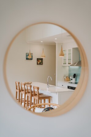 A modern kitchen with white cabinets, a central island, and wooden chairs. - Exquisitely Spacious 3-bed Home (Canberra)