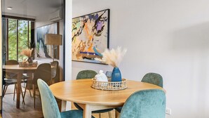 A modern dining area with a wooden table and teal upholstered chairs. - Contemporary 1-bed in the Heart of St Kilda (Melbourne)