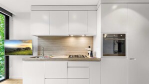 A modern kitchen with white cabinetry, a built-in oven, and a large window with a view of greenery. - Contemporary 1-bed in the Heart of St Kilda (Melbourne)